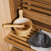 Wooden bucket and ladle on a wooden bench in a sauna with a towel and 'Helius' branding.